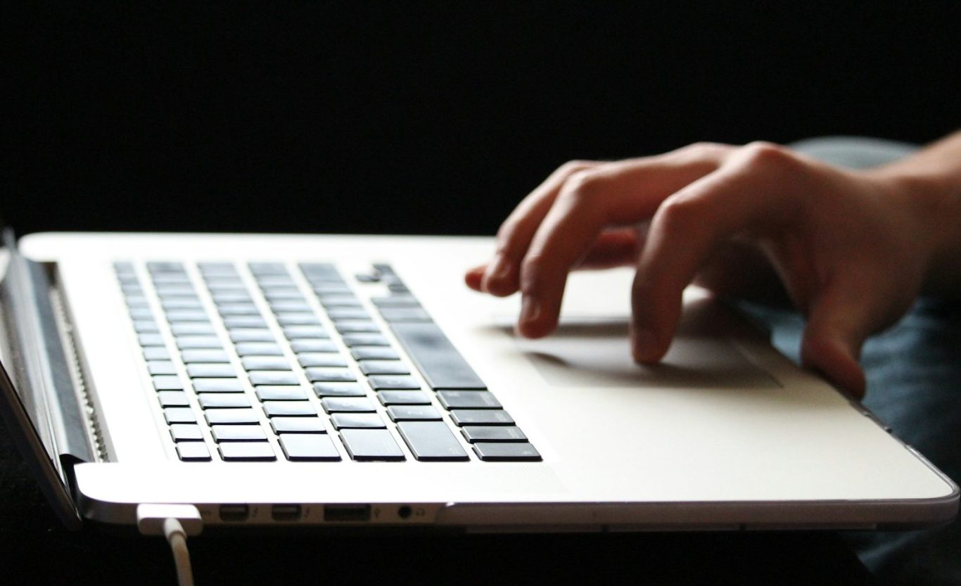 A hand typing on a laptop keyboard against a black background. A hand typing on a laptop keyboard with a black background.